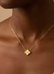Gold necklace with a flower pendant on a person wearing a beige top against a beige background