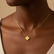 Gold necklace with a flower pendant on a person wearing a beige top against a beige background