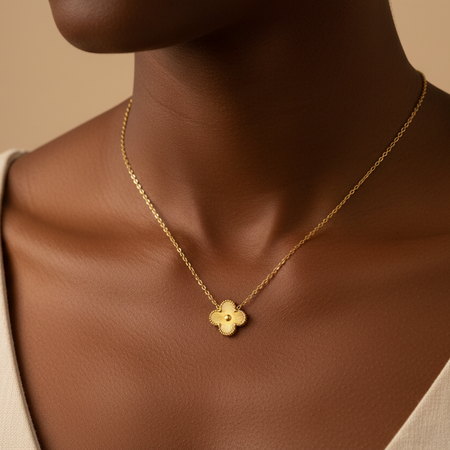 Gold necklace with a flower pendant on a person wearing a beige top against a beige background